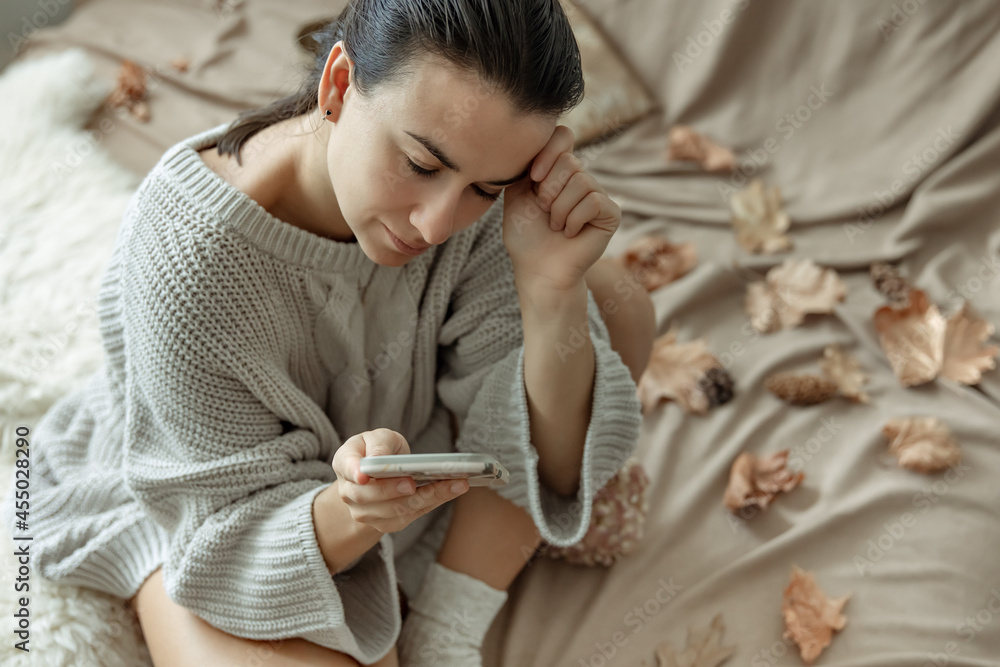 Young woman in a knitted sweater with a phone in her hands in bed.