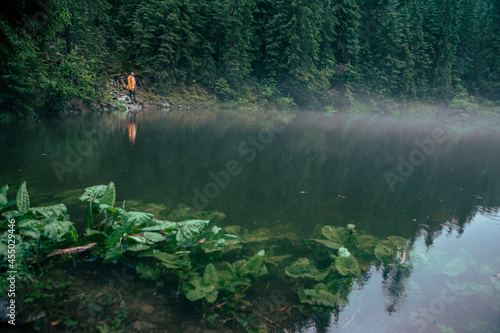 man hiker in yellow raincoat looking at mountain lake