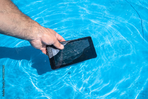 A man's hand takes out a black smartphone from the water of a blue pool. Moisture ingress into the phone.