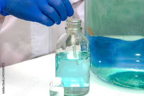 a laboratory assistant in the laboratory draws liquid from a bubble with a pipette next to vessels of other sizes