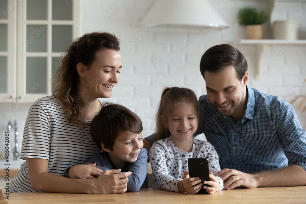 Happy millennial parents and kids using mobile phone for video call from home, talking to family together. Couple and sibling children chatting online with grandparents. Family connection concept Happy millennial parents and kids using mobile phone for video call from home, talking to family together. Couple and sibling children chatting online with grandparents. Family connection concept