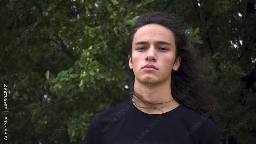 aggressive looking long black haired young protest man standing scowling in front of wire netting aggressive looking long black haired young protest man standing scowling in front of wire netting