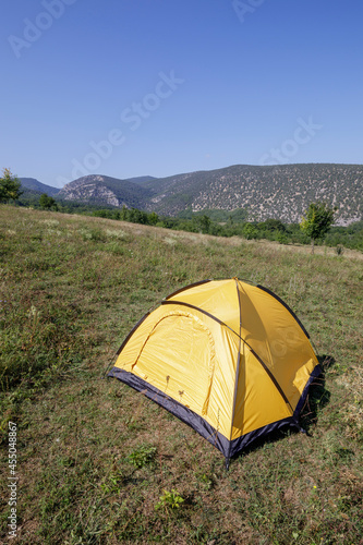 Yellow tourist tent in the grass in a meadow in the mountains, camping and tourist house for hiking.