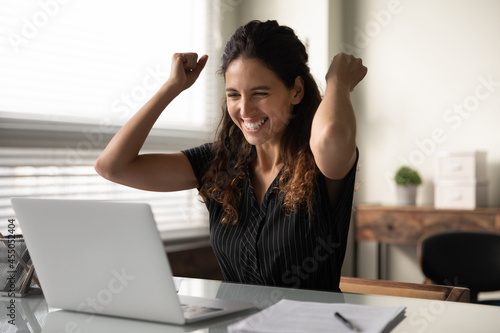 Slika na platnu Happy excited millennial businesswoman in casual excited with good news at laptop, looking at screen, celebrating win, achieve, approved loan, making yes hand gesture