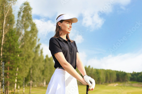 Professional female golfer holding golf club on field and looking away. Young woman standing on golf course on a sunny day.