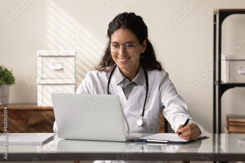 Принти на полотні Happy young female GP doctor using laptop, making video call, reading electronic medical records