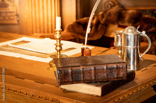 Ancient book with candleholder and feather quill pen on antique wooden desk in luxury working room. Literature and history reading concept