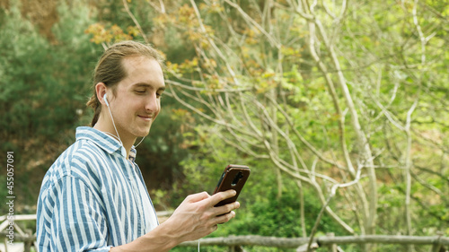 Young handsome hipster man using smartphone and listening music with earphones in the forest