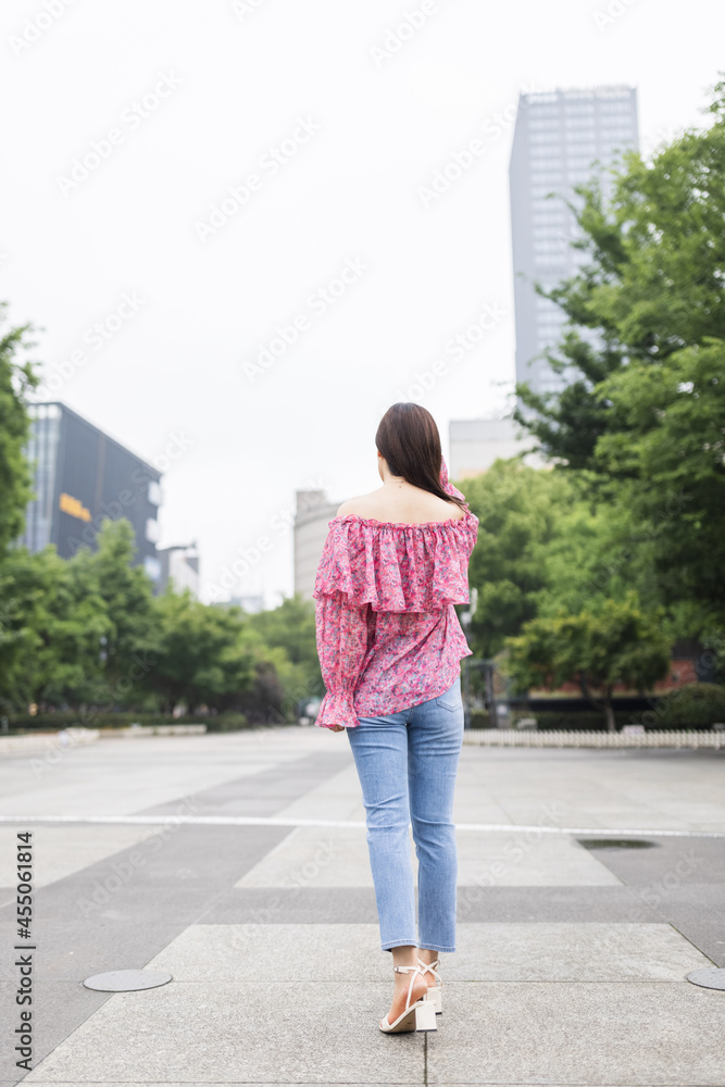 Portrait of young asian woman from behind wearing stylish casual clothing and walking outdoor in city. Happy stylish woman enjoys life Portrait of young asian woman from behind wearing stylish casual clothing and walking outdoor in city. Happy stylish woman enjoys life