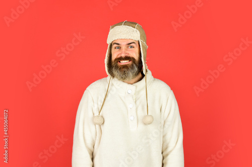 Bearded man wear hat with ear flaps red background. Soft furry accessory. Caring fur garments. Bearded funny hipster. Winter fashion concept. Warm hat for cold weather. Sheep fur. Perfect accessory © be free