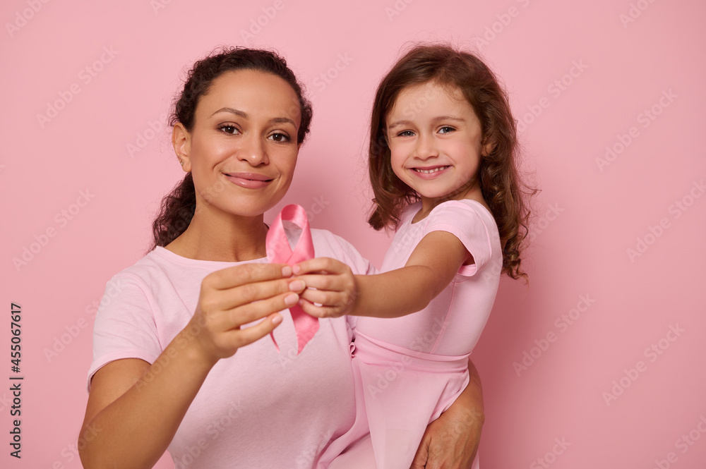 Two generations of women, mom and daughter hugging each other, holding pink ribbon, Breast Cancer awareness day symbol, showing support and solidarity to patients and cancer survivors. Women's health Two generations of women, mom and daughter hugging each other, holding pink ribbon, Breast Cancer awareness day symbol, showing support and solidarity to patients and cancer survivors. Women's health