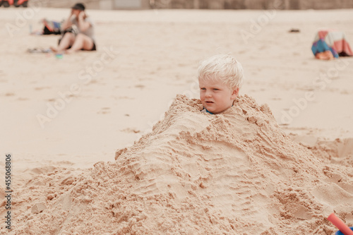 Фотография Little boy buried in pile of sand on the beach