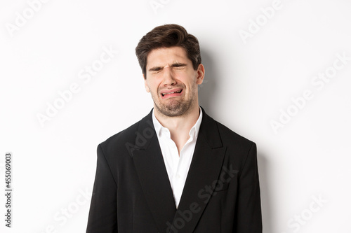 Close-up of miserable man in suit, crying and sobbing, feeling sad, standing against white background photo