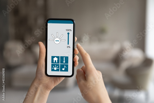 Close up young woman holding telephone with smart home app on screen, iot, virtual assistant, distant indoors temperature change or light regulation, remote climate control system, music control.