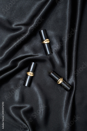 Two lipsticks on black wavy silk background. Luxury makeup product. Satin fabric texture. Dark elegant rich backdrop. Delicate design. Shine decoration christmas material. Tender art drape