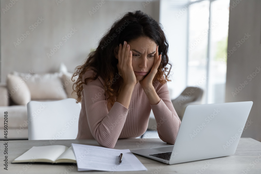 Stressed young hispanic woman looking at computer screen, stack with difficult task, feeling confused getting email with bad news, suffering from headache due to long work on online project at home. Stressed young hispanic woman looking at computer screen, stack with difficult task, feeling confused getting email with bad news, suffering from headache due to long work on online project at home.
