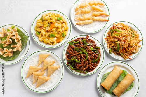Chinese food on a white tablecloth table. Beef with garlic sauce, chicken curry, spring rolls, noodles with vegetables, prawns with shrimp.