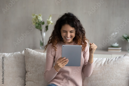 Overjoyed emotional young latina woman looking at digital tablet screen, celebrating online lottery auction betting giveaway win, feeling excited reading email with amazing news, internet success.