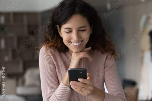 Happy beautiful young latin woman using mobile software applications, enjoying communicating distantly in social network typing message, reading email with pleasant news, shopping or playing game.