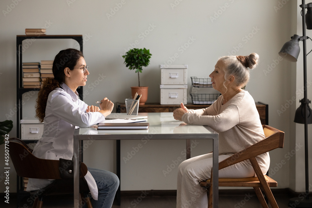 Positive young female doctor and old patient meeting and talking in office or at home. Therapist, physician giving advice to senior woman at appointment, answering to health problem complaints Positive young female doctor and old patient meeting and talking in office or at home. Therapist, physician giving advice to senior woman at appointment, answering to health problem complaints