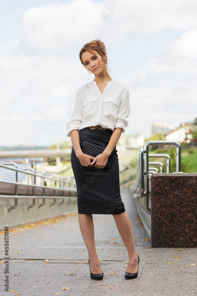 Young fashion business woman in white shirt and pencil skirt with clutch bag Stock Adobe Stock