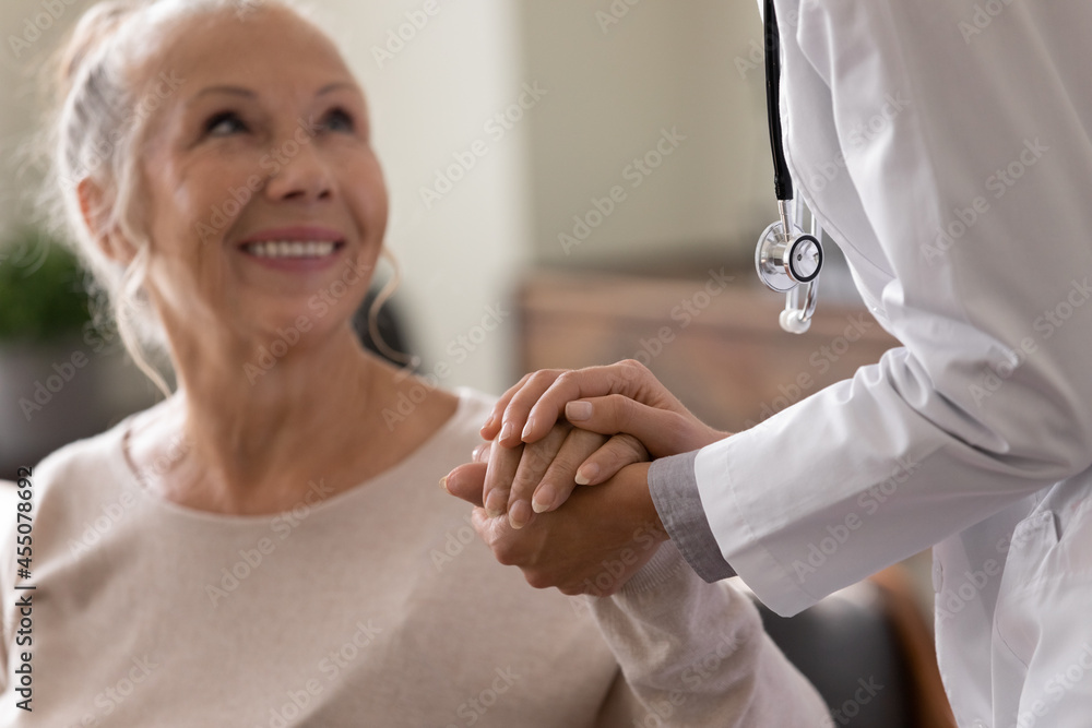 Obraz premium Happy senior woman visiting doctor, getting optimistic news after medical checkup, therapy. Therapist holding hand of old patient, giving hope, support, congratulating on goor treatment result