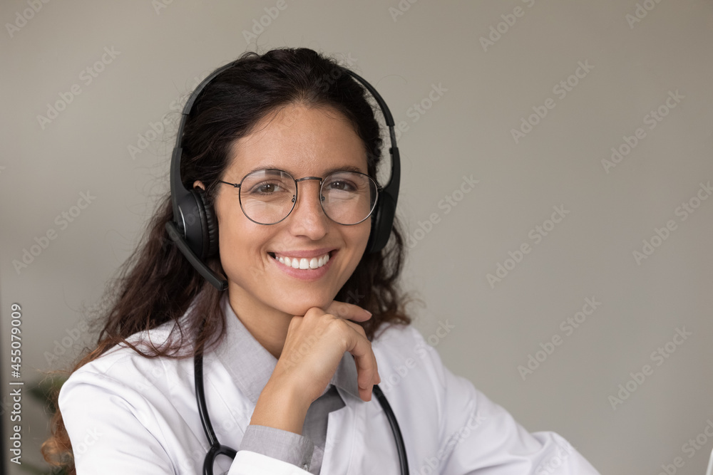 Portrait of happy young female doctor wearing headset and glasses, looking at camera, smiling. General practitioner, medical professional, physician giving online virtual telehealth consultation Portrait of happy young female doctor wearing headset and glasses, looking at camera, smiling. General practitioner, medical professional, physician giving online virtual telehealth consultation