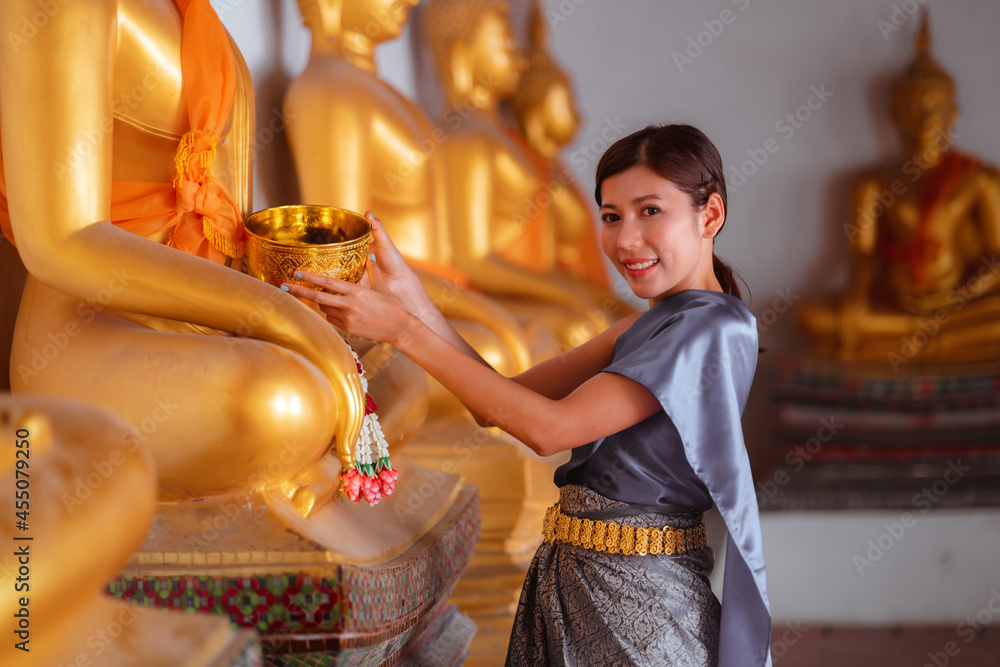 Asian woman wearing a Thai national costume bathing of buddha during the Songkran Festival in Thailand. Thai New Year's Day. Thai tradition.