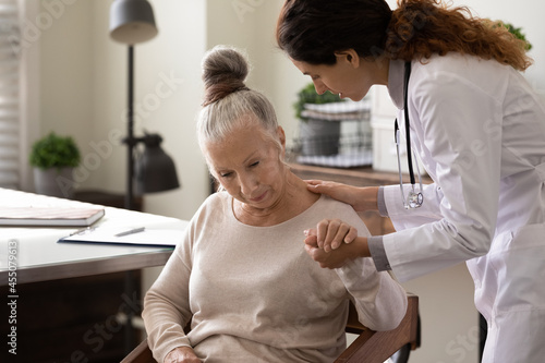 Serious young doctor helping elder patient to cope with bad news, serious diagnosis, holding hand of woman, giving comfort, support, empathy. Medic care, geriatric health care concept