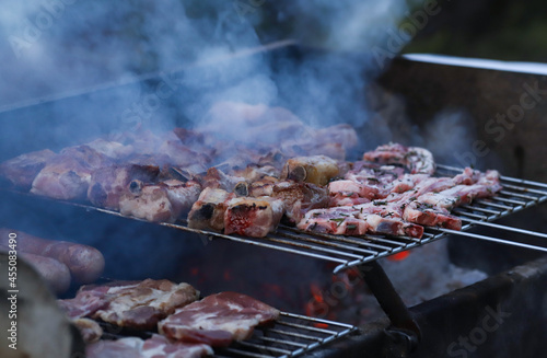 Outdoor barbecue with mixed meats in cooking, blue smoke.