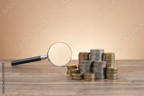 Coins with various values stacked on the wooden table with a magnifying glass at the back  photo