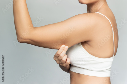 Konstfotografi Close-up of a young caucasian blonde woman grabbing skin on her upper arm with excess fat isolated on a gray background