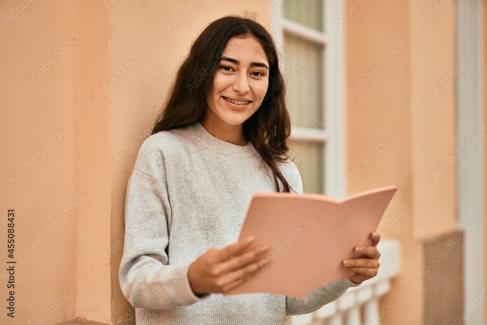 Young middle east student girl smiling happy reading book at the city. Young middle east student girl smiling happy reading book at the city.