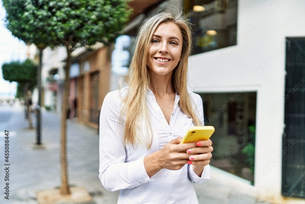 Beautiful blonde woman smiling happy outdoors on a sunny day using smartphone Beautiful blonde woman smiling happy outdoors on a sunny day using smartphone