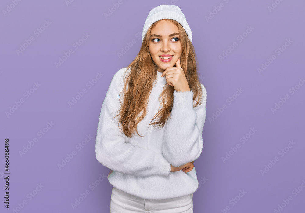 Young caucasian girl wearing wool sweater and winter cap with hand on chin thinking about question, pensive expression. smiling with thoughtful face. doubt concept. Young caucasian girl wearing wool sweater and winter cap with hand on chin thinking about question, pensive expression. smiling with thoughtful face. doubt concept.
