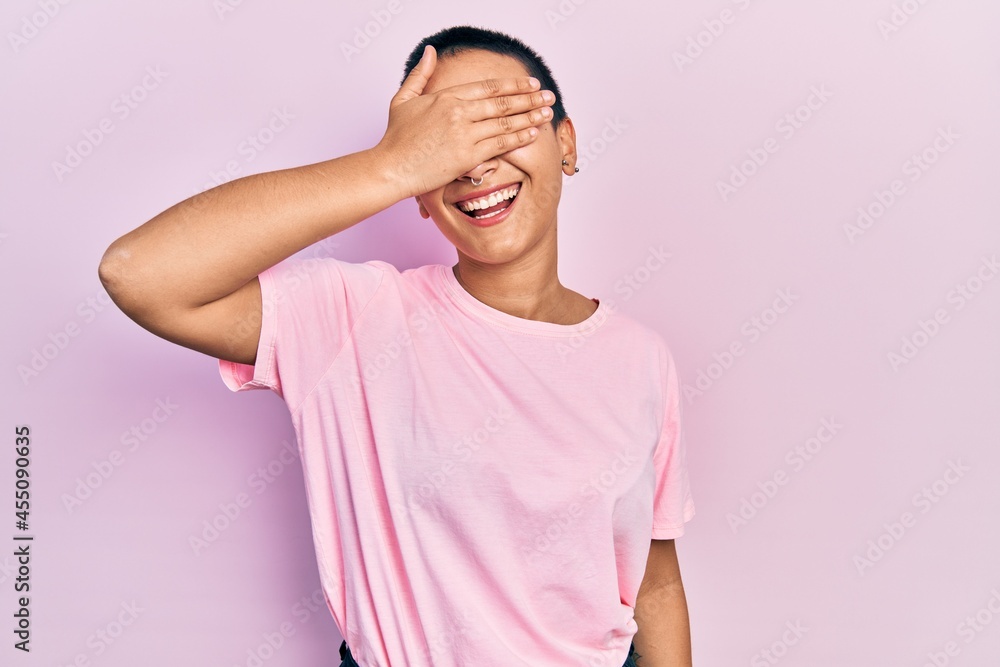 Beautiful hispanic woman with short hair wearing casual pink t shirt smiling and laughing with hand on face covering eyes for surprise. blind concept. Beautiful hispanic woman with short hair wearing casual pink t shirt smiling and laughing with hand on face covering eyes for surprise. blind concept.