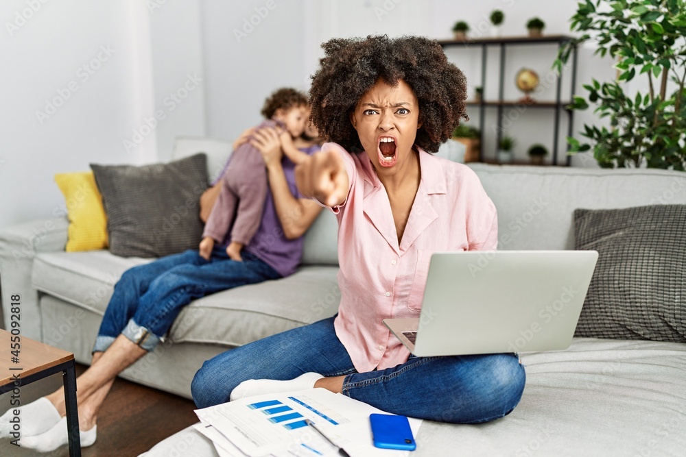 Mother of interracial family working using computer laptop at home pointing displeased and frustrated to the camera, angry and furious with you