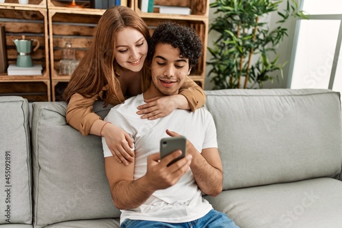 Young couple smiling happy and hugging sitting on the sofa at home.