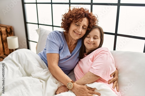 Mother and down syndrome daughter relaxing confortable on the bed hugging with love