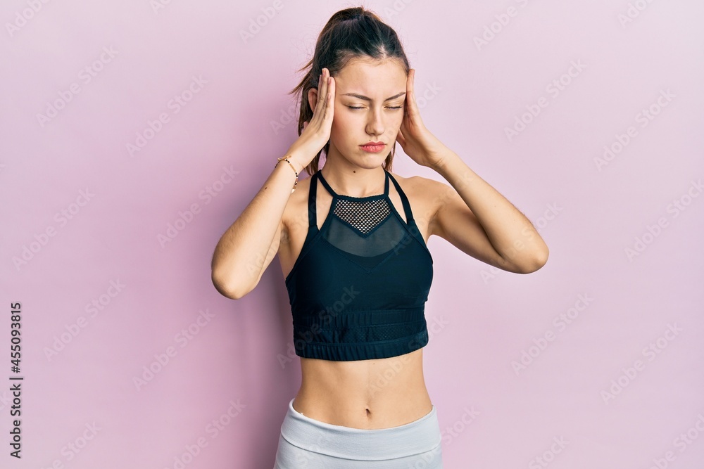 Young brunette woman wearing sportswear suffering from headache desperate and stressed because pain and migraine. hands on head. Young brunette woman wearing sportswear suffering from headache desperate and stressed because pain and migraine. hands on head.
