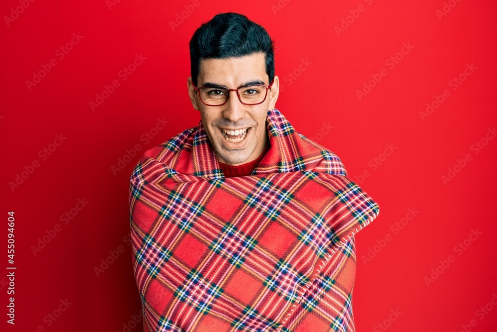 Handsome hispanic man wrapped in a red warm red blanket smiling and laughing hard out loud because funny crazy joke. Handsome hispanic man wrapped in a red warm red blanket smiling and laughing hard out loud because funny crazy joke.