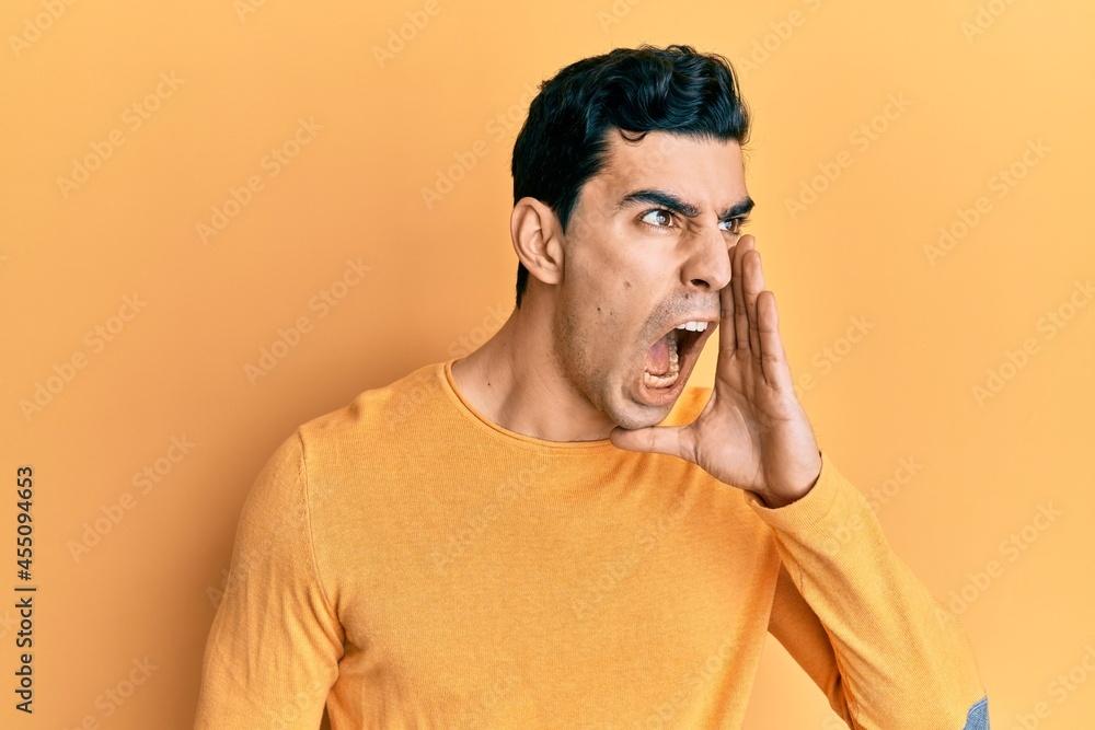 Handsome hispanic man wearing casual clothes shouting and screaming loud to side with hand on mouth. communication concept. Handsome hispanic man wearing casual clothes shouting and screaming loud to side with hand on mouth. communication concept.
