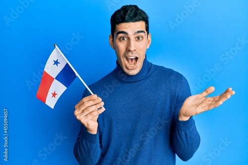 Handsome hispanic man holding panama flag celebrating achievement with happy smile and winner expression with raised hand
