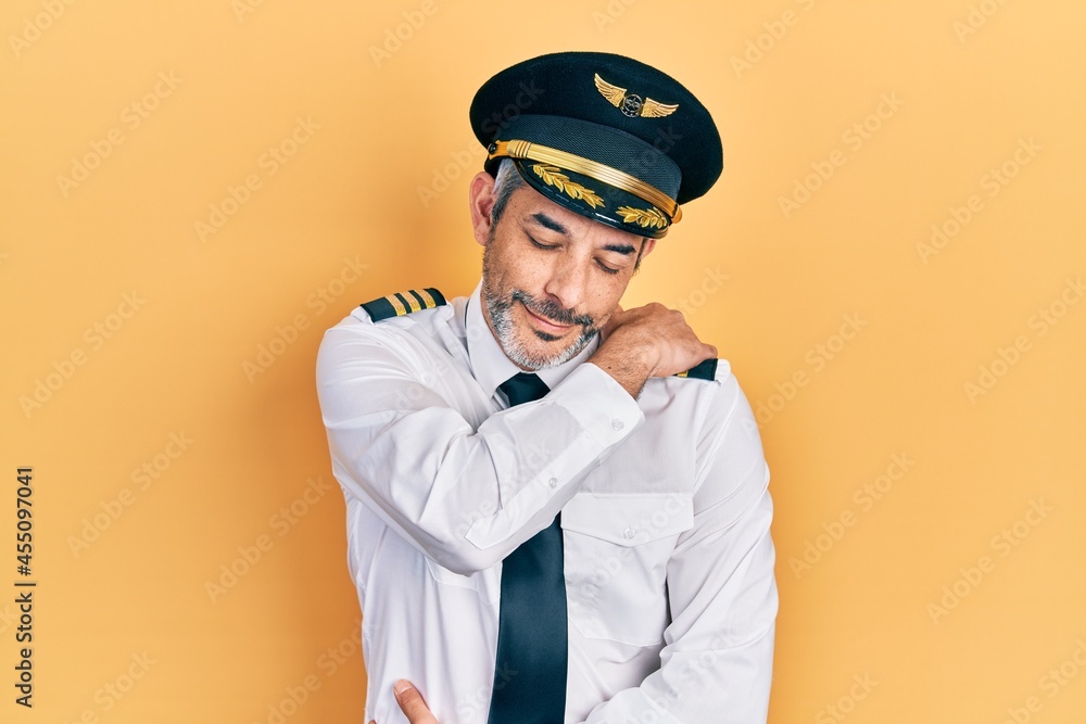 Handsome middle age man with grey hair wearing airplane pilot uniform hugging oneself happy and positive, smiling confident. self love and self care Handsome middle age man with grey hair wearing airplane pilot uniform hugging oneself happy and positive, smiling confident. self love and self care