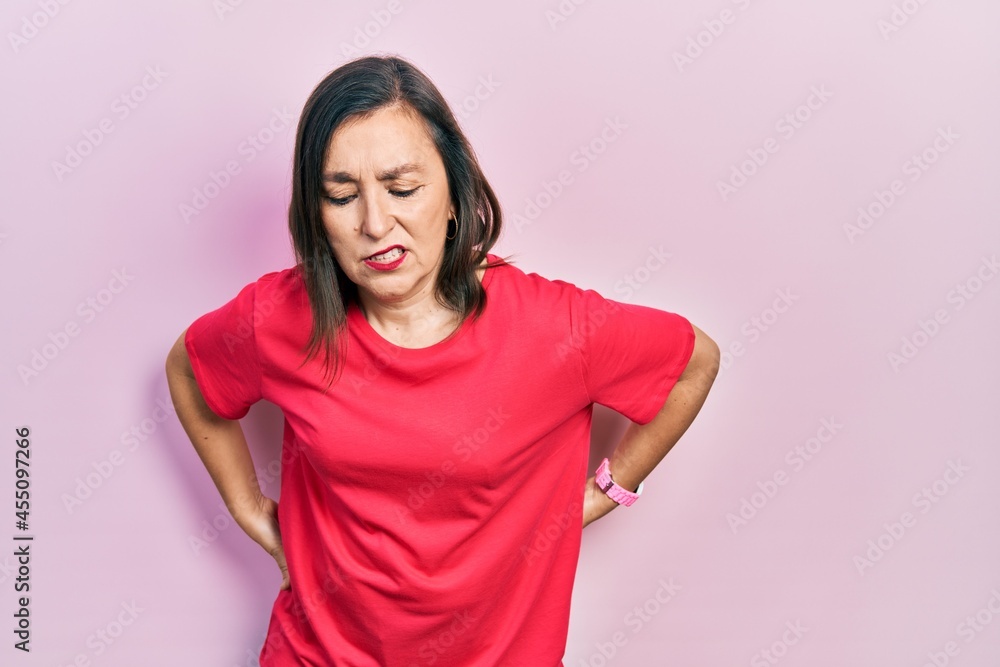 Middle age hispanic woman wearing casual clothes suffering of backache, touching back with hand, muscular pain Middle age hispanic woman wearing casual clothes suffering of backache, touching back with hand, muscular pain