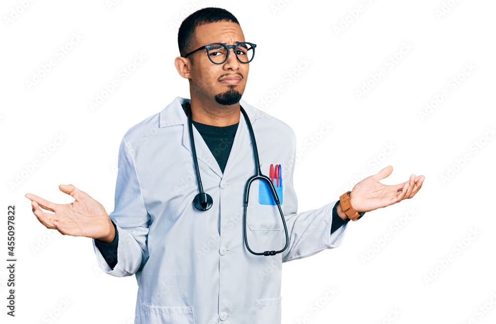 Young african american man wearing doctor uniform and stethoscope clueless and confused with open arms, no idea concept. Young african american man wearing doctor uniform and stethoscope clueless and confused with open arms, no idea concept.