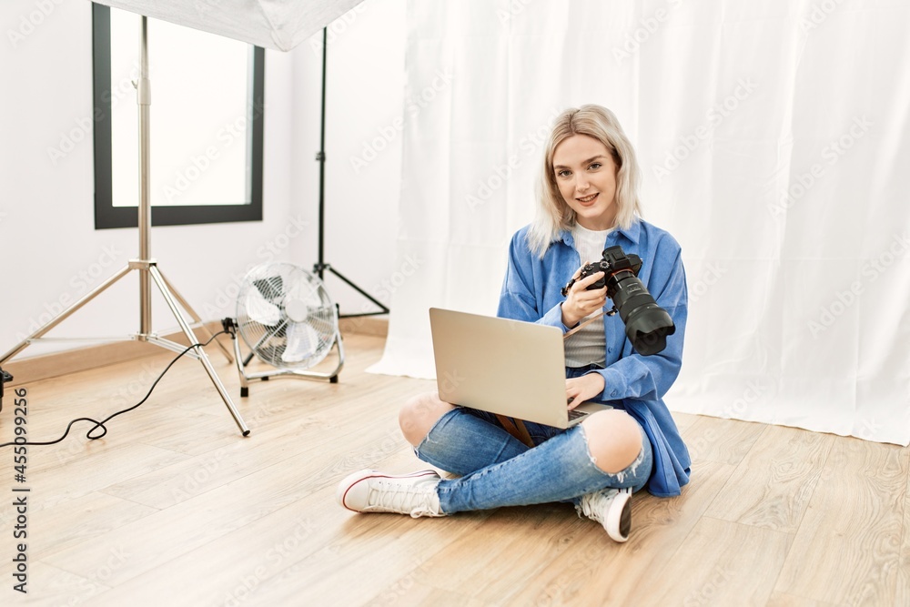 Beautiful blonde woman working as professional photographer at photography studio sitting on the floor checking photos on computer laptop Beautiful blonde woman working as professional photographer at photography studio sitting on the floor checking photos on computer laptop