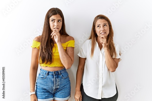 Mother and daughter together standing together over isolated background thinking worried about a question, concerned and nervous with hand on chin