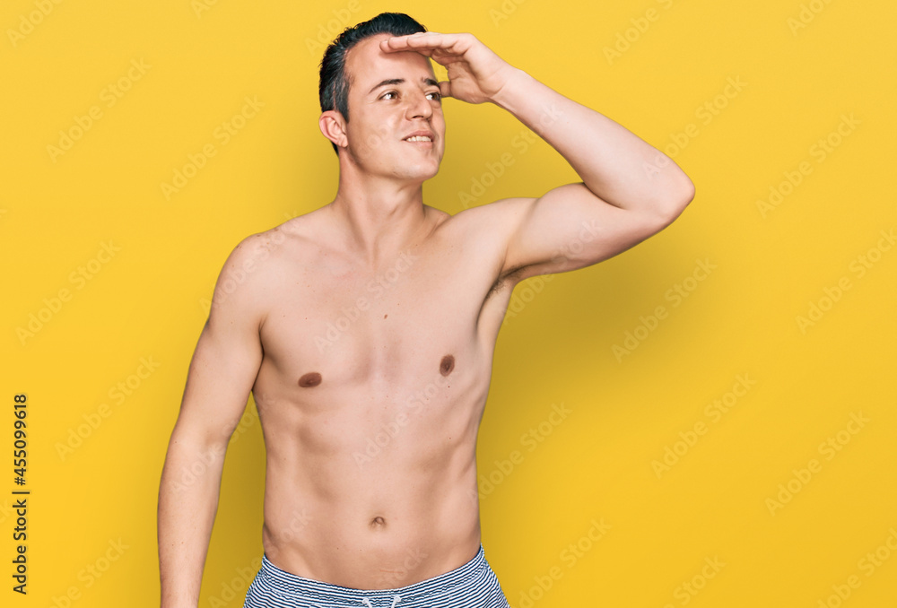Handsome young man wearing swimwear shirtless smiling confident touching hair with hand up gesture, posing attractive and fashionable