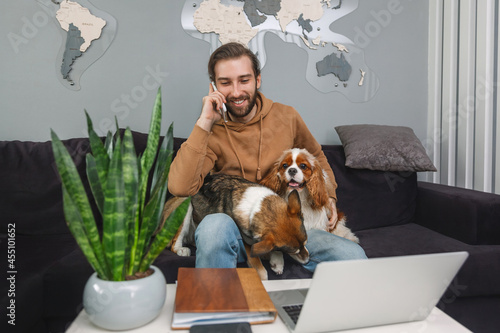 Photography Young handsome man talking on cell phone at home and hugging his dogs